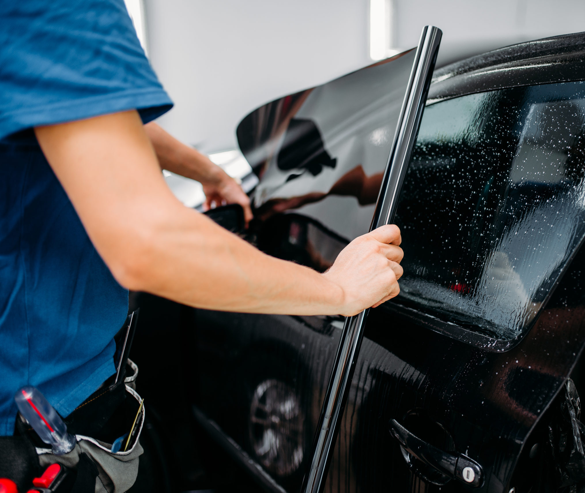 Male specialist applying car tinting film, installation process, tinted auto glass installing procedure